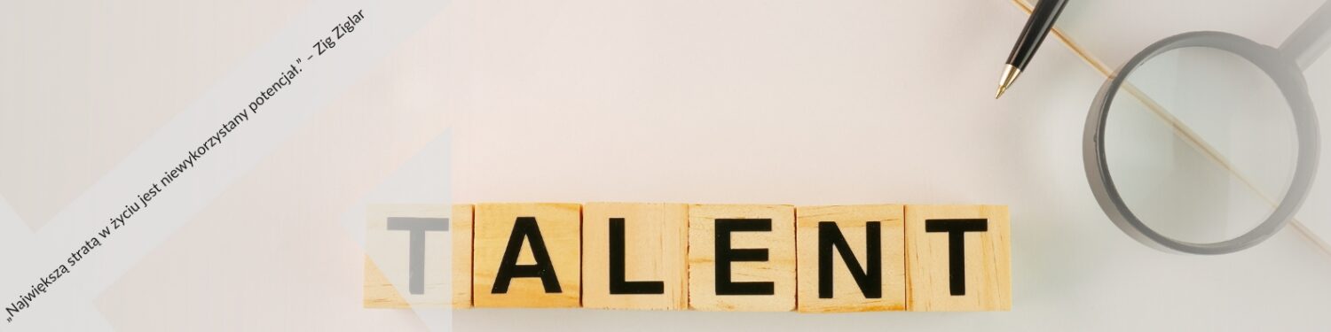 Zdjęcie przedstawia drewniane klocki ułożone w słowo "TALENT" na jasnym tle. Obok znajdują się lupę i pióro, symbolizujące analizę i kreatywność. W tle widoczny jest fragment papieru z cytatem Ziga Ziglara: "Największa strata w życiu to niewykorzystany potencjał".